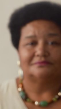 Afrika kökenli, kıvırcık saçlı ve renkli aksesuarlı bir kadının kameraya bakarken çekilmiş portre fotoğrafı.