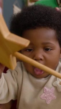 Tahta oyuncakla oynayan, tanınmayan bir anne tarafından tutulan kıvırcık saçlı sevimli Afrikalı Amerikalı kızın dikey görüntüsü.