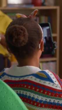 Afro-Amerikalı bir kızın tripoda akıllı telefonu tutarken ve ailesinin videosunu çekerken dikey çekim.