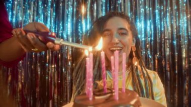 Partide tanınmayan bir arkadaşın mumları üflemesini bekleyen heyecanlı, Kafkasyalı bir kadının orta boy yakın çekimi.