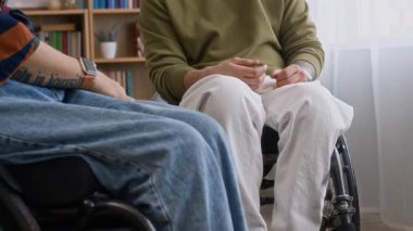 Tekerlekli sandalyedeki gülümseyen beyaz bir adamın yavaşça öne eğip, kadın arkadaşına yumruk tokuşturması, evde oturup sohbet etmesi ve gülmesi.