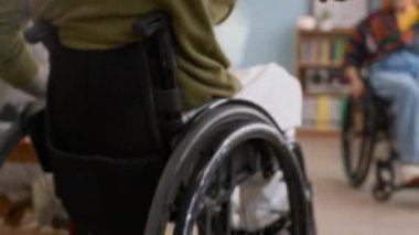 Tekerlekli sandalyedeki mutlu beyaz arkadaşların birbirini beşlikle selamlamalarını, sonra kucaklaşmalarını ve sohbete başlamalarını, sıcak oturma odasında birlikte vakit geçirmelerini.