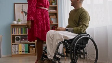 Genç siyahi bir kadının tekerlekli sandalyedeki genç beyaz bir adamı kucaklarken, uzun zaman sonra yakın arkadaşıyla buluşurken ve evinde rahat bir şekilde sohbet ederken elde çekilmiş bir fotoğraf.