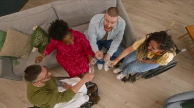 Modern oturma odasındaki koltukta oturmuş arkadaşlarıyla şampanya bardaklarını tokuşturup, evde birlikte vakit geçirmekten keyif alan neşeli genç çiftin yavaş çekimleri.