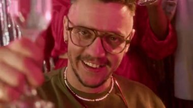 Bir grup neşeli çoklu etnik arkadaş kameraya bakıyor şampanya kadehlerini kaldırıyor, parlak folyo perdelere karşı dans ediyor ve süslü partinin tadını çıkarıyorlar.