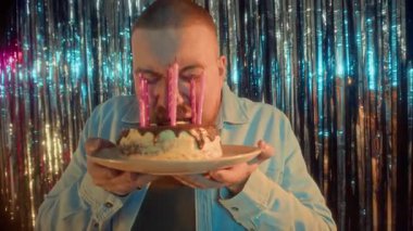 Kafkas asıllı genç bir adamın elinde mumlarla doğum günü pastası tutarken ve onu büyük bir gülümsemeyle ısırırken, partide doğum gününü kutlarken.