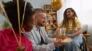 Doğum günü pastasındaki tüm mumları üfleyen mutlu beyaz adamın yavaş çekimini yakınlarda arkadaşlarının elinde balonlarla evinde gülerken yakınlaştır.