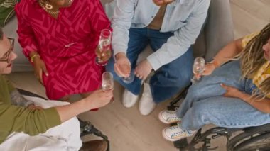 Yüksek açılı, çeşitli genç arkadaşlar ve tekerlekli sandalye kullanıcılarından oluşan neşeli yavaş çekim bardaklarını tokuşturarak, şampanya içerek ve evde eğlenerek.