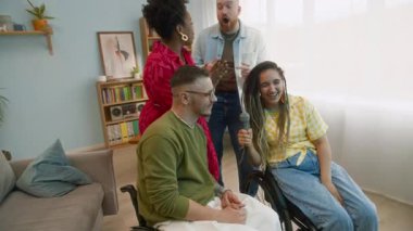 Bir grup çok ırklı arkadaş ve tekerlekli sandalye kullanıcısı, mikrofona karaoke şarkıları söyleyerek, dans ederek ve gülerek birlikte eğleniyorlar.