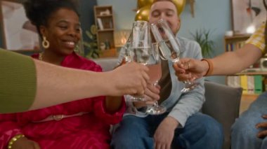 Oturma odasındaki koltukta oturan, tekerlekli sandalyeli arkadaşlarıyla şampanya bardaklarını tokuşturup, evde bir araya gelen mutlu, etnik çeşitliliğe sahip çiftin yavaş çekimleri.