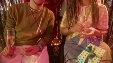 Tekerlekli sandalyedeki genç beyaz çiftin yavaş yavaş çekilen portresini kaldırarak arkadaki neşeli arkadaşlarıyla kameraya bakıp doğum günü partisini kutlamak için şampanya kadehlerini kaldırırlar.