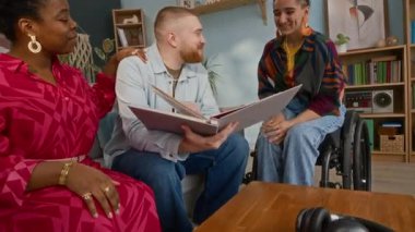 Tekerlekli sandalyedeki genç beyaz kadının çok ırklı arkadaşlarıyla sohbet edip eğlendiği, fotoğraf albümüne bakıp birlikte geçirdiğimiz güzel anılardan bahsederken çekilmiş bir fotoğraf.