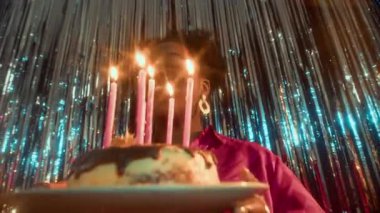 Doğum günü pastası tutan mumlara bakarken genç siyahi bir kadının dilek tuttuğu yavaş çekim.