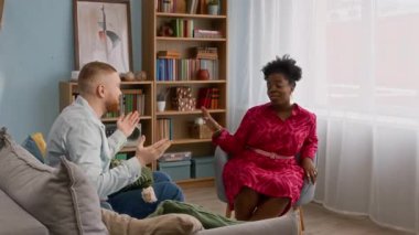 Engelli genç beyaz adam, çok ırklı genç arkadaşlarına katılıyor. Oturma odasında sohbet ediyor, selamlaşıyor ve konuşuyor. Birlikte vakit geçirmekten mutlu.