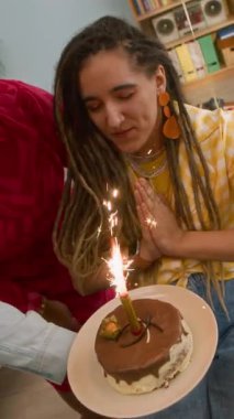 Doğum günü pastasının önünde mum ışığında dilek tutan mutlu, genç, beyaz bir kadının dikey, yavaş çekimi. Doğum gününü evinde, yakın arkadaşlarıyla birlikte kutluyor.