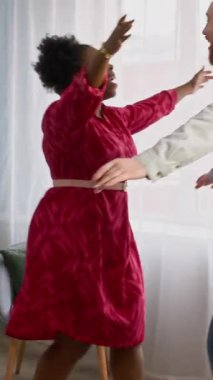 Genç mutlu siyahi kadının, rahat modern oturma odasında genç beyaz erkek arkadaşını karşılayıp sıcak duygusal kucaklaşma ve sohbet başlatmasının dikey ve yavaş çekimi.