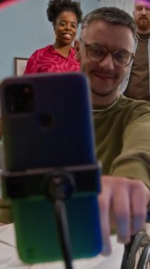 Tekerlekli sandalyedeki genç adam tripodla cep telefonuna yaklaşıyor ve kendini kameraya kaydediyor. Mutlu arkadaşlarla dans ediyor, evde birlikte eğleniyor.