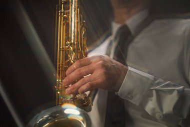 Sahne ışıkları altında caz çalan erkek müzisyenlerin ellerinde parlak altın saksafona yakın çekim, ışık dağılım efekti, boşluk kopyalama