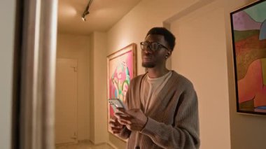 Modern sanat galerisindeki kulaklıklarda müze ses rehberini dinlerken Afrika kökenli genç bir adamın akıllı telefon kullanarak resim çekerken elde çekilmiş bir fotoğrafı.