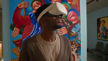 Sanal gerçeklikte sergilenen soyut sanat eserleri koleksiyonunu incelerken VR kulaklık takan genç Afrikalı Amerikalı adamın orta boy yakın çekimi.