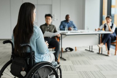 Tekerlekli sandalyedeki genç kadının arka plan portresi ofisteki çeşitli iş adamlarına konuşma yapıyor, boşluğu kopyalıyor.