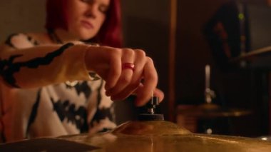 Punk kızı yakın plan çekimde, kızıl saçlı kız müzik stüdyosunun provası sırasında davul setiyle nazikçe zil sesi ayarlıyor.