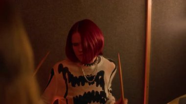 Yavaş çekim, yakın plan punk kızı boyalı kızıl saçlı, koyu renk ses geçirmez müzik stüdyosunda davul çalarken.