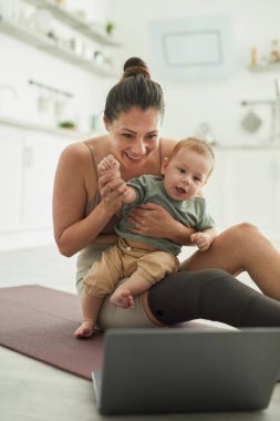 Engelli modern annenin dikey portresi. Bebeği kucağında tutuyor ve video konuşmalarıyla el sallıyor.