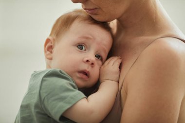 Annesinin kollarında kameraya bakan sevimli kızıl saçlı bebek portresi, ebeveynlik ve annelik kavramı.