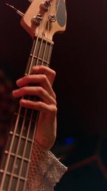 Açık renkli, uzun kollu tişörtlü, dört telli bas gitarlı, tanınmayan bir elin dikey yakın çekimi.