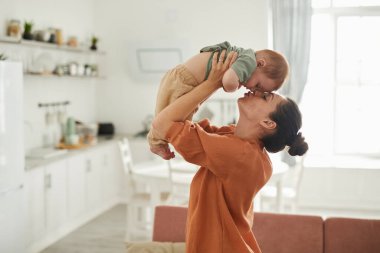 Yandan bakan mutlu genç annenin portresi bebeğiyle rahat bir evde oynuyor, boşluğu kopyalıyor.