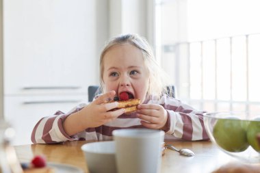 Evinde ailesiyle kahvaltı ederken tatlı waffle yiyen Down sendromlu tatlı bir kızın portresi.