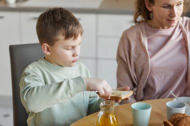 Evde ailesiyle kahvaltıda reçelli sandviç yapan sevimli bir çocuğun yüksek açılı portresi.