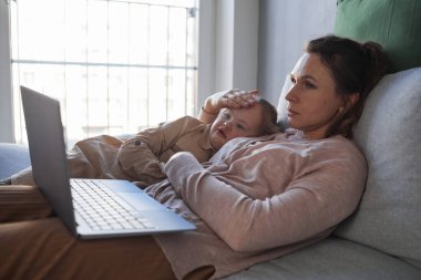 Şefkatli annenin kanepeye uzanması Down sendromlu kızını kucaklaması ve dizüstü bilgisayarla video izlemesi, boşluğu kopyalaması.