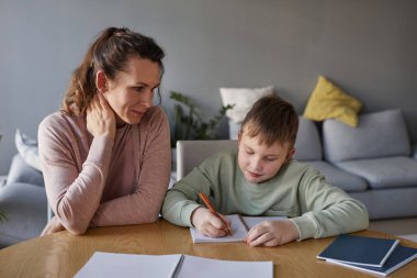 Gülümseyen bekar annenin portresi oğlunun oturma odasında ödev yapmasına yardım ediyor, boşluğu kopyalıyor.