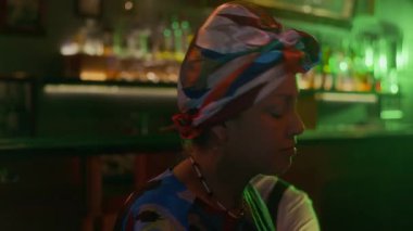 Piyano, saksafon ve davullarla dinamik caz üçlüsü loş ışıklı barda canlı performans sergiliyor, neon renklerle banyo yapıyor.