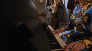 Dişi caz piyanisti, melodiye dalmış, saksafoncu ve perküsyonist olarak ona eşlik ediyor, sıcak ışıklandırılmış alanda ahenkli ve anlamlı bir canlı performans yaratıyor.