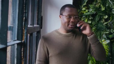 Zeki giyimli ve gözlüklü genç Afro-Amerikan işadamlarının orta derecede yavaşlığı telefonda konuşurken proje detaylarını tartışıyorlar yeşil duvarın önünde duruyorlar.