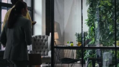 Zarif ve şık gündelik giysiler içinde genç erkek ve kadın çalışma arkadaşları modern yeşil ofise giriyor, konferans masasında birlikte iş projesinde çalışmaya başlıyorlar.