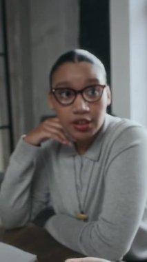 Orta boy, kendine güvenen Afrikalı Amerikalı genç iş kadınının modern ofis toplantısında yanında oturan tanınmayan meslektaşıyla projeyi tartışırken.