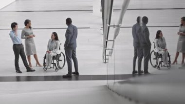 Tekerlekli sandalyede oturan Kafkas iş kadını ve üç farklı meslektaşının modern ofis molasında iletişim kurdukları yüksek açıdan görülüyor.