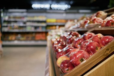 Markette sergilenen temiz ambalajlarda taze elmalar parlak ışık ve diğer meyve ve sebzelerle dolu raflarla dolu bölümde üretiliyor.