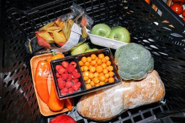 Çan biberi, ahududu, brokoli, elma ve domateslerle çevrili ekmek de dahil olmak üzere çeşitli taze yiyeceklerle dolu alışveriş arabası.