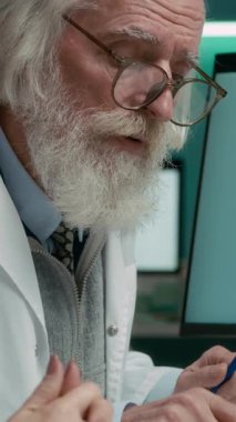 Laboratuvar önlüklü üst düzey Kafkas erkek araştırmacının dikey pozisyonu PC 'nin önünde oturuyor ve ekranda veri analizi çizelgesi oluşturan yapay zeka asistanının yardımını kullanıyor.