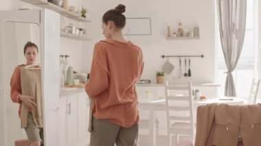 Orta yaşlı, çekici beyaz kadın bacak protezi takmış evde aynanın önünde duruyor ve dışarı çıkmak için kıyafet seçiyor.