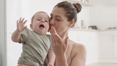 Orta yaşlı, güzel, beyaz bir kadının mutfakta elinde küçük oğluyla onu öperken ve onunla oynarken görüntüsü.