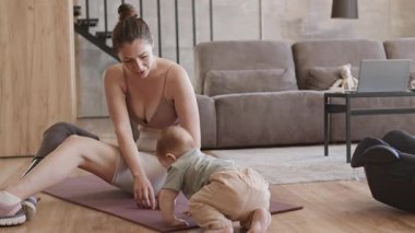 Eğitimden sonra apartmandaki lastik paspasın üzerinde oturan ve yanında emekleyen tatlı bebekle oynayan sportif anne kiti.