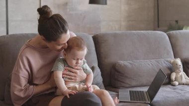 Oturma odasında elinde bebekle oturan ve onu başından öpen bacak protezi takılı güzel bir kadın.