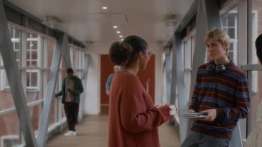 Sınıf dışında neşeli bir şekilde sohbet eden bir grup genç üniversitenin koridorunda dikilip erkek profesörü selamlıyor.