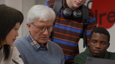 Üst düzey erkek profesörün dizüstü bilgisayarı işaret eden gözlük taktığı orta ölçekli bir fotoğraf. Üniversitedeki çalışma oturumunda bir grup genç öğrenciye projenin detaylarını açıklarken.